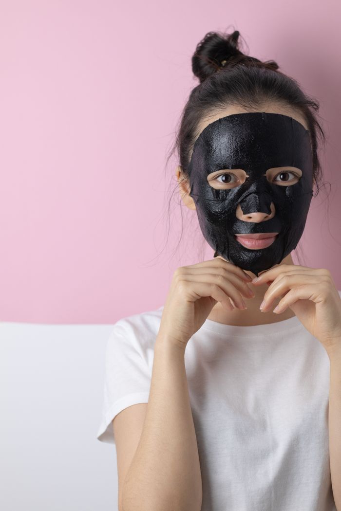 A woman applying a black sheet facial mask, promoting self-care and skincare.